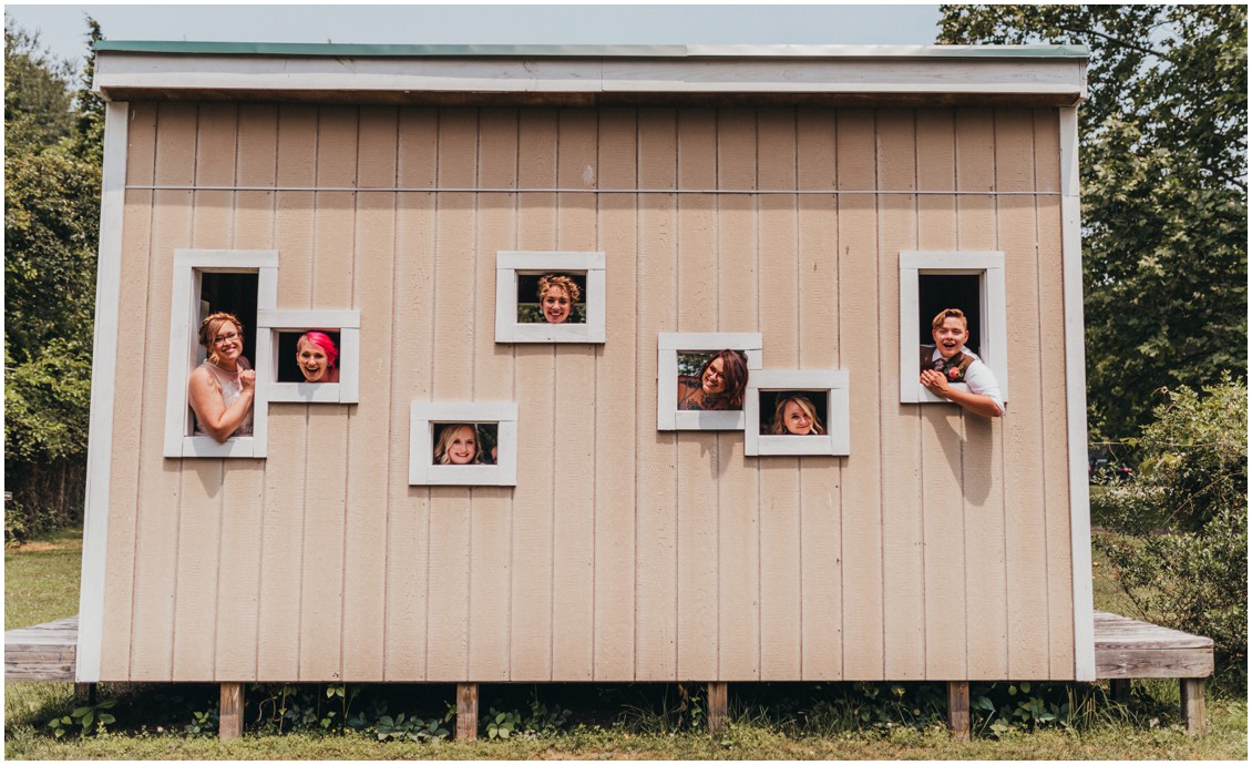 Newly weds with friends posing out of little windows in the side of a small building. | My Eastern Shore Wedding | 