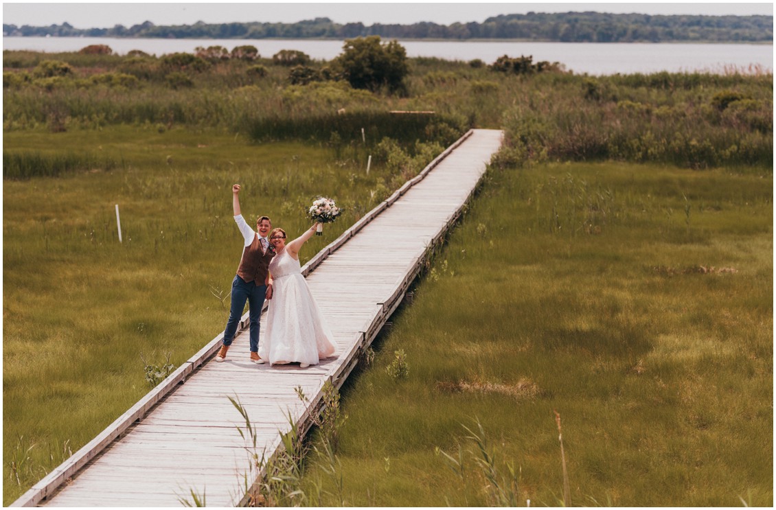 Married couple on long wooden dock with arms raised. | My Eastern Shore Wedding | 