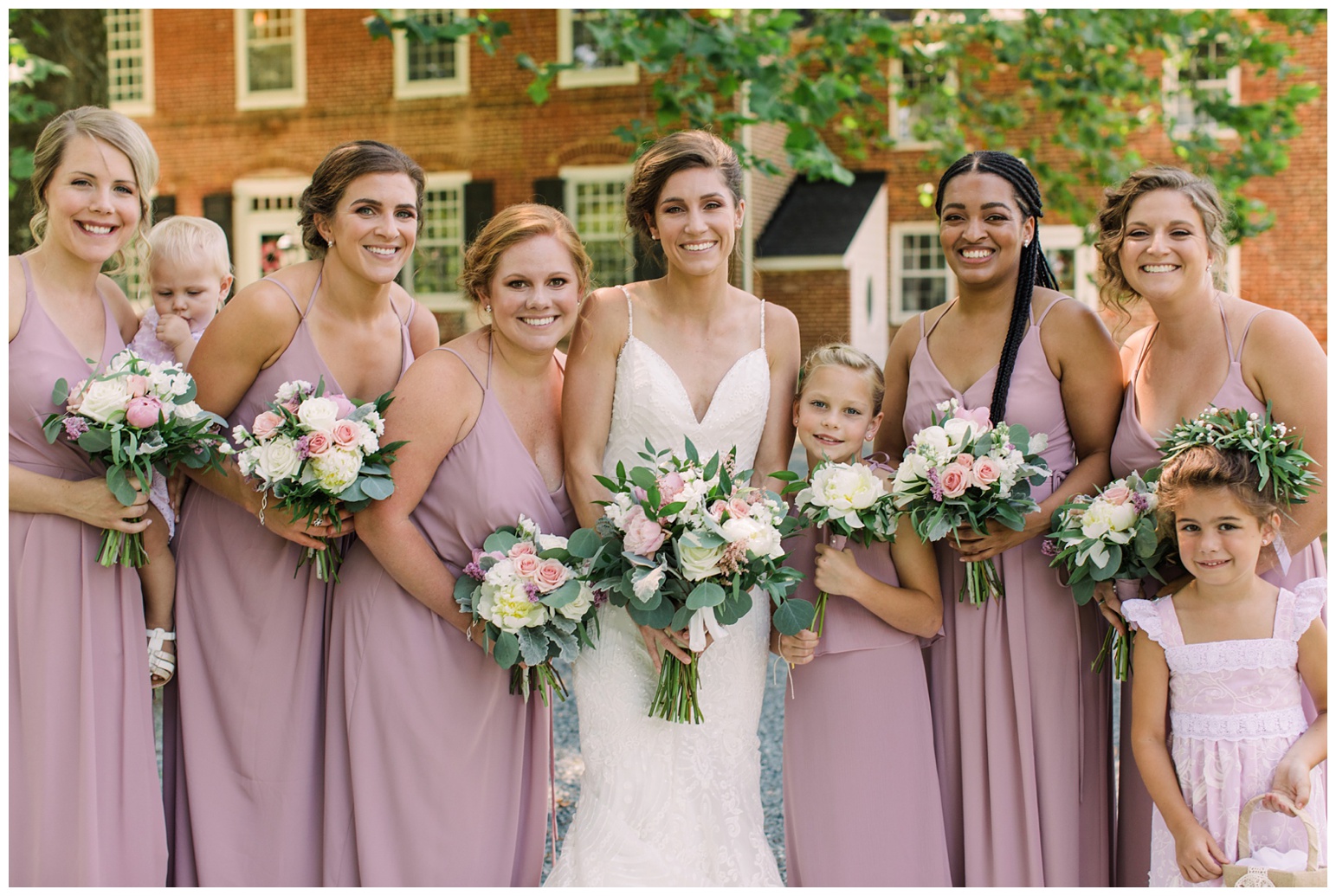 worsell manor wedding in the summer - warwick md - now featured on My Eastern Shore Wedding - coastal - sea - nautical - eastern shore - inspired wedding ideas and inspo - photo of bride bridesmaids and flower girl outdoors in front of brick manor style building - one flower girl wearing flower crown carrying basket