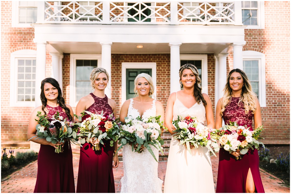 Bride and bridesmaids in red dresses in front of mansion| Kingsbay Mansion| My Eastern Shore Wedding