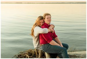The bride to be hugs her fiance from behind as they watch the sun set over the bay. | My Eastern Shore Wedding | Cassidy MR. Photography