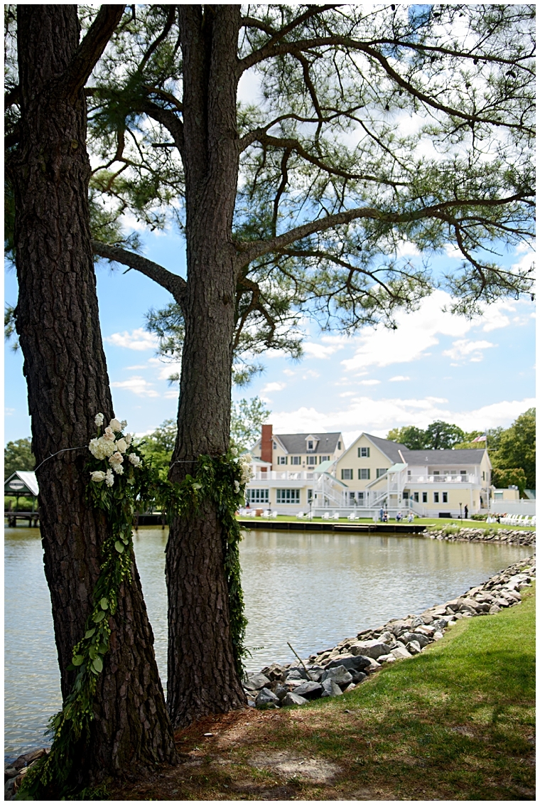 A waterfront ceremony site at The Oaks is shaded by trees and detailed with florals by Seaberry Farms