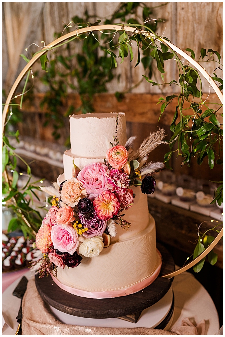A four tiered wedding cake decorated with pink florals is displayed at the reception at Worsell Manor.