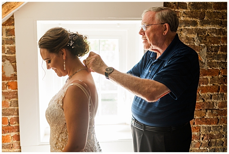 The father of the bride helps his daughter put on her necklace before her wedding ceremony at Worsell Manor.