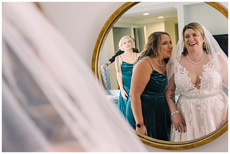 The bride takes a first look at herself in her gown and veil with her bridesmaids