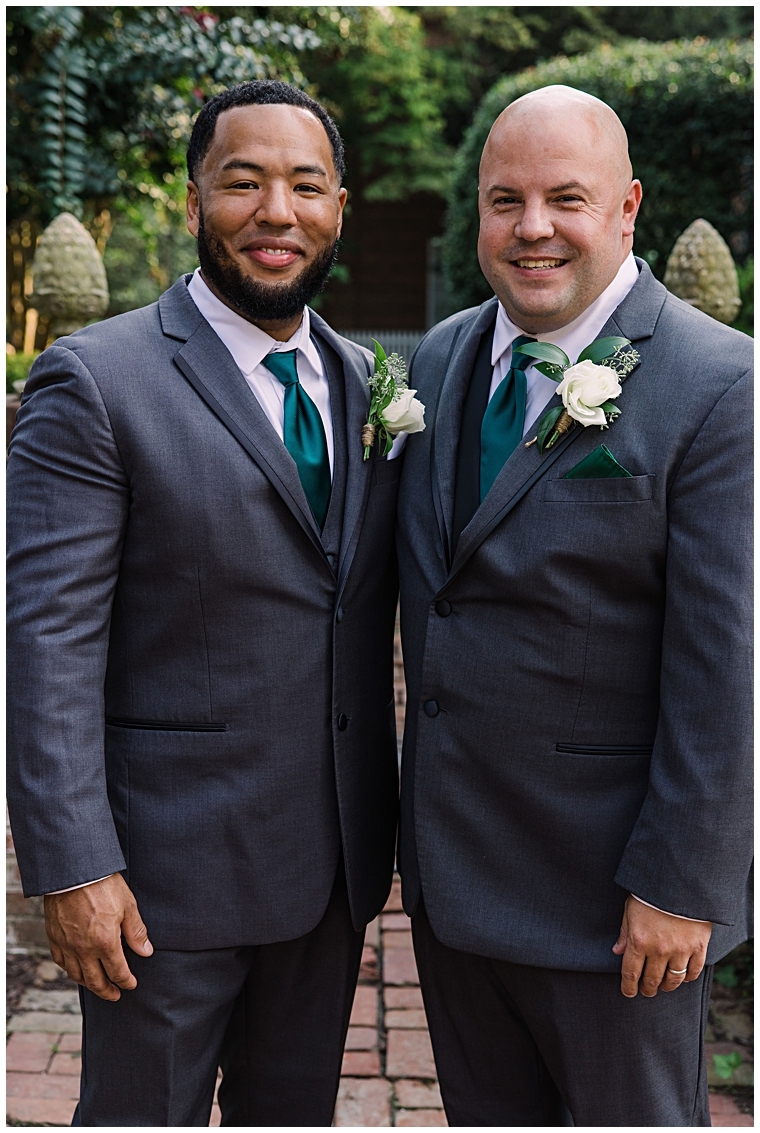 The groom is dressed in a dashing grey suit with a teal tie and white rose florals by Sweetbay Designs at their Tidewater Wedding
