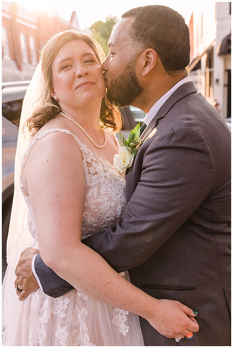 Dressed in a beautiful lace gown, the bride receives a sweet kiss on the cheek from her new husband