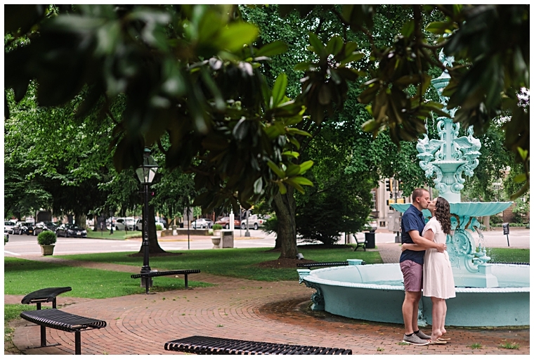 Standing in front of the fountain in the town square, the couple embraces in a kiss | Laura's Focus Photography
