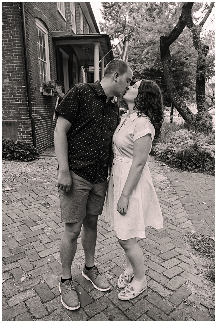The couple shares a kiss on the sidewalk for a beautiful black and white portrait by Laura's Focus Photography