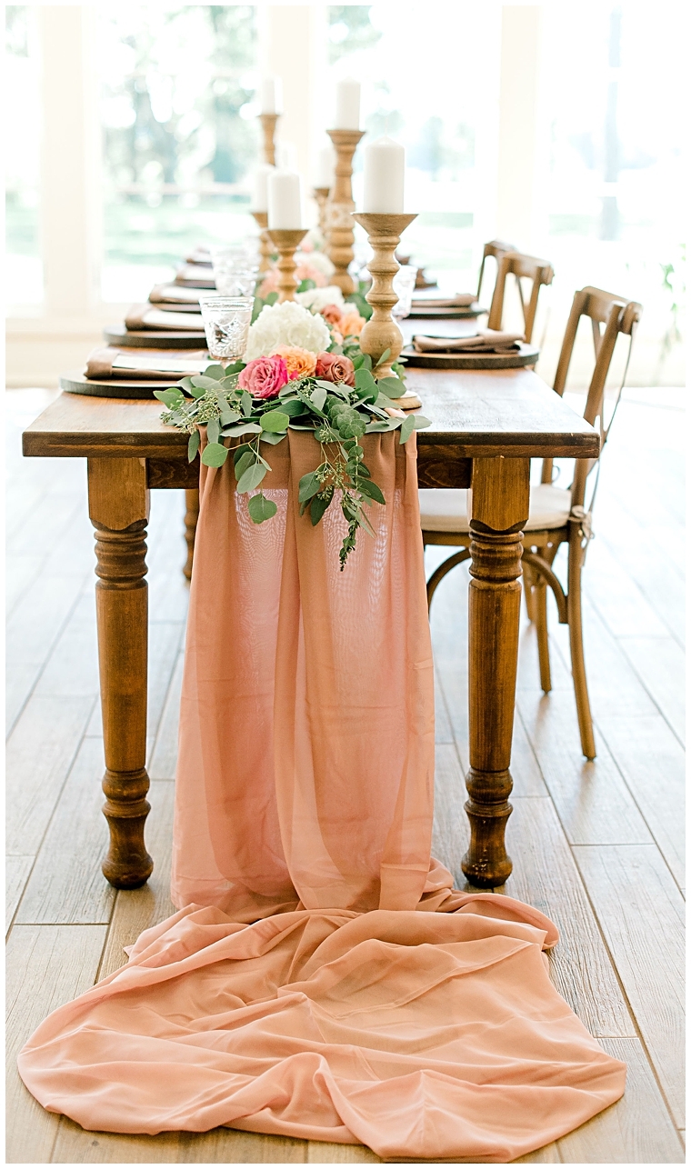 A blush table runner dresses this natural wood head table detailed with greenery and florals