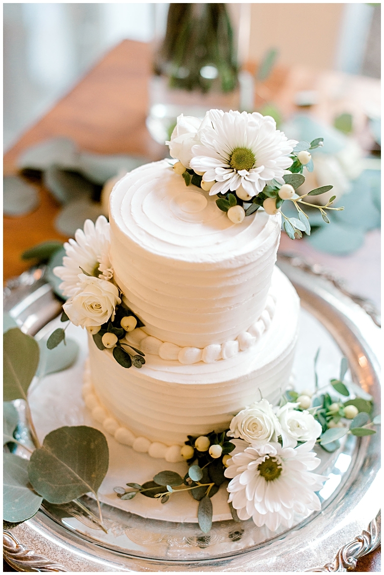 A two tiered white wedding cake with florals and greenery