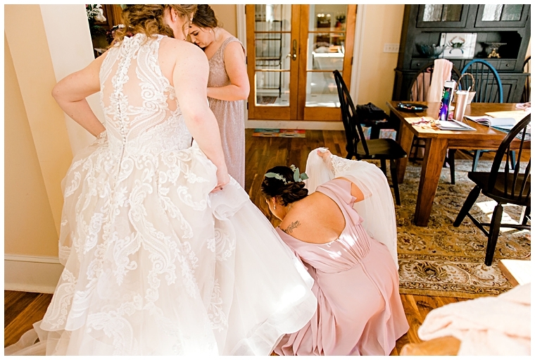 Bridesmaids help the bride with her gown and shoes.