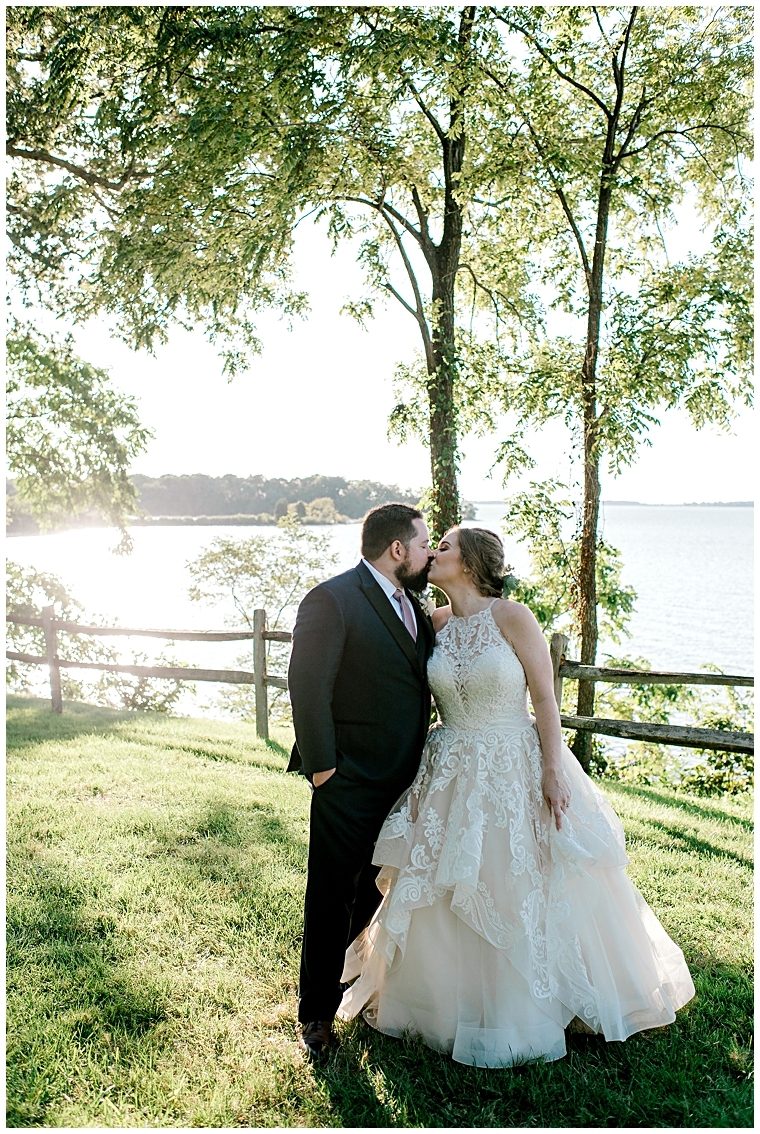 The bride and groom embrace in a sweet kiss at the waterfront at Great Oak Manor