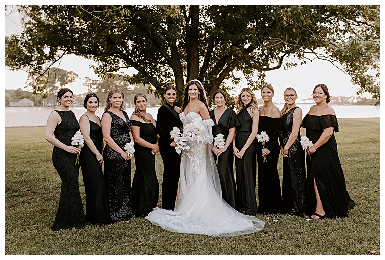 Donned in black gowns the bridesmaids surround the bride for a portrait in the dreamy sunlight as it breaks through the cloud cover  | My Eastern Shore Wedding