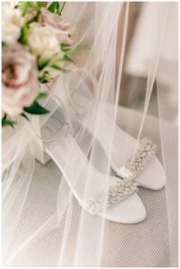 The bride's shoes are staged with her bridal bouquet and veil for a detail shot