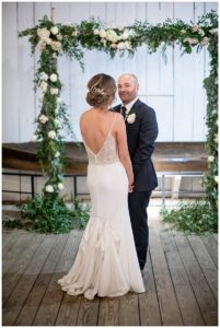 The archway is decorated with greenery and white roses for this Maritime Museum wedding with florals by Seaberry Farms