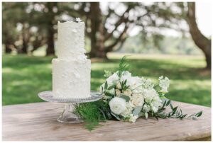 A two tiered white wedding cake with a bridal bouquet by Three Little Buds Florals