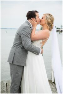 The bride and groom embrace in a romantic kiss on the waterfront