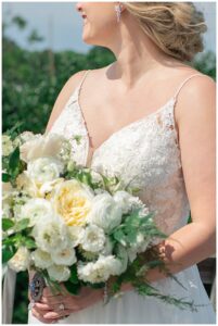 Dressed in a white lace gown and detailed with white roses for her big day, the bride poses for a bridal portrait