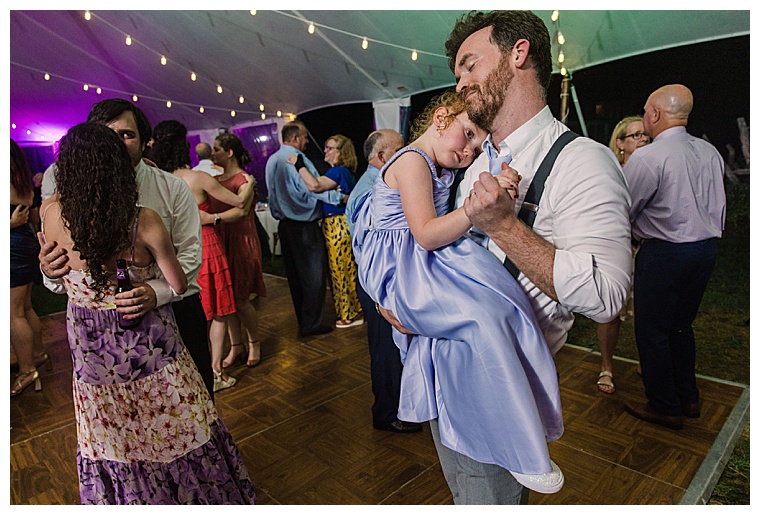 Groomsmen dances with a flower girl as she rests her tired head on his shoulder at the end of the night
