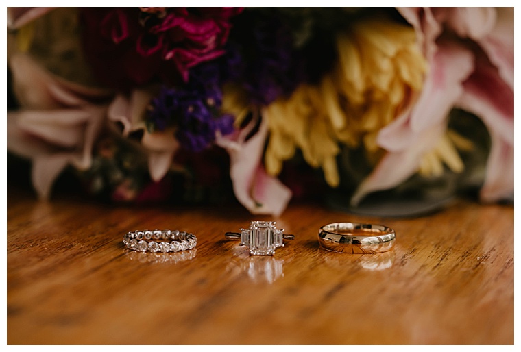 A detail image of the engagement ring and both wedding bands with florals as the beautiful backdrop