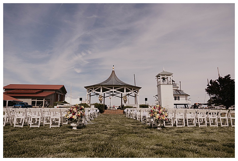 The lawn at the Chesapeake Bay Maritime Museum is set up with elegant white ceremony chairs and florals for an exchanging of vows that will take place under the gazebo