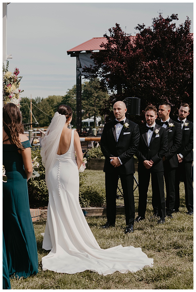 The bride, dresses in a simple but elegant white fit and flare gown detailed with pearl buttons, meets her groom at the altar for their ceremony