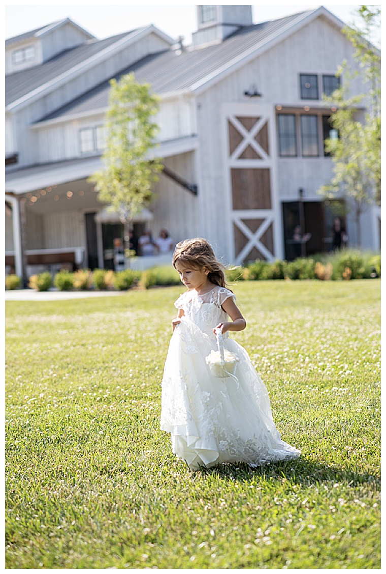 An adorable flower girl in a white flower gown with a white basket leads the way for the bride as they enter the ceremony