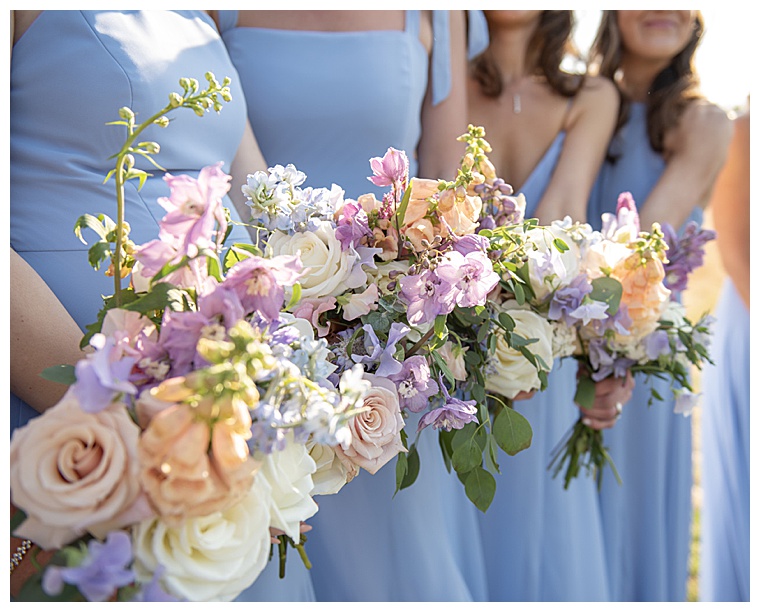 Bridesmaids with bouquets of white roses and pastel details to match a mismatched set of dusty blue dresses
