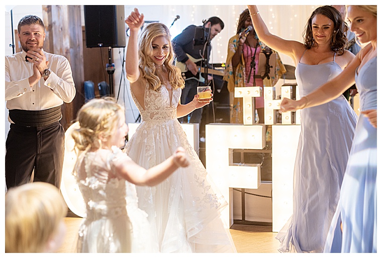 Bride and bridesmaids dance with the flower girl on the dance floor during the reception