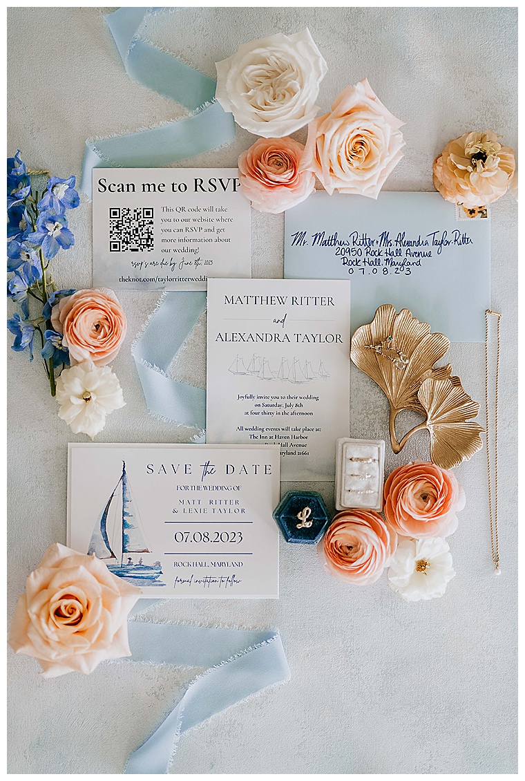 The blue and white invitation suite is staged surrounded by lovely white roses and detailed with the bride's jewelry for this Haven Harbour Wedding Day