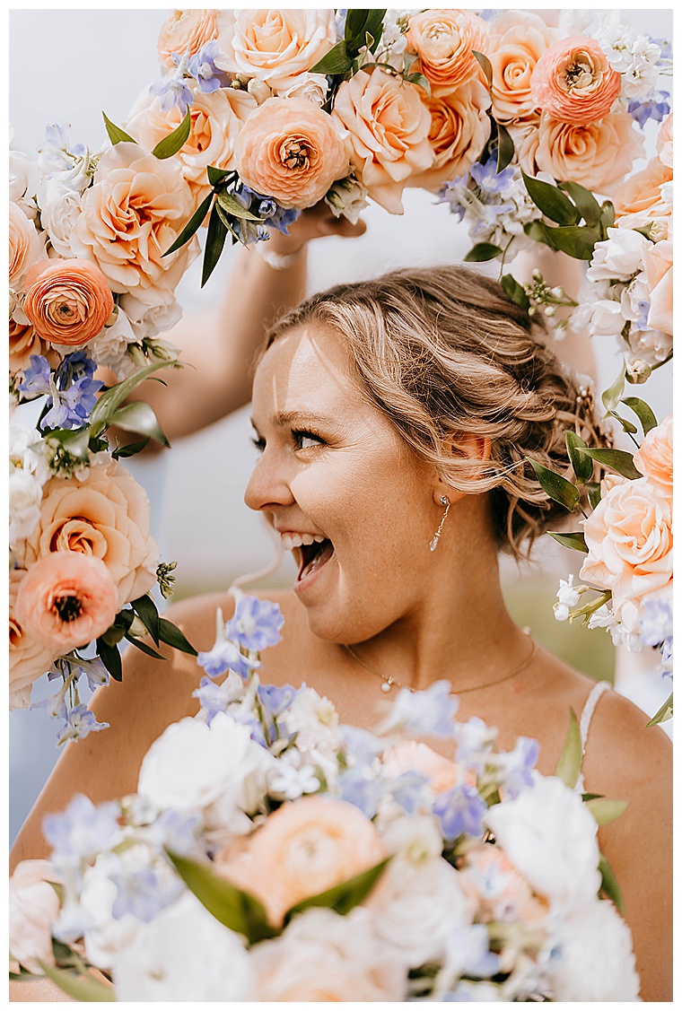 This bubbly bride poses for her close up at her bridesmaids frame the portrait with their rose bouquets