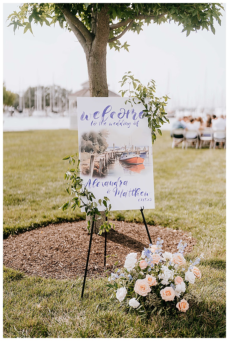 A custom made welcome sign for Lexi and Matt's Haven Harbour wedding detailed with greenery and a watercolor design of the docks