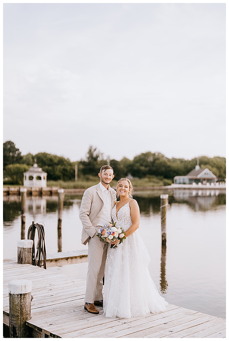 The bride and groom pose for a stunning portrait on the dock at the Inn at Haven Harbour overlooking the waterfront with a quaint gazebo in the background