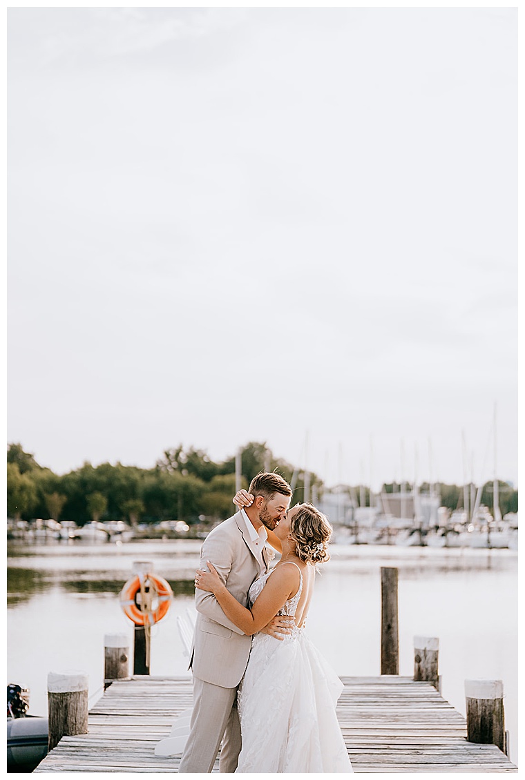 The newlyweds embrace in a romantic kiss on the dock overlooking a beautiful golden hour sunset at the Inn at Haven Harbour