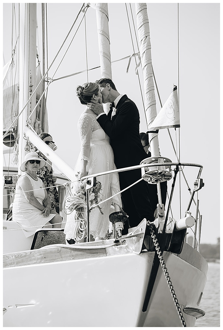 The bride and groom share a romantic kiss on the bow of the ceremony sailboat to conclude a romantic ceremony