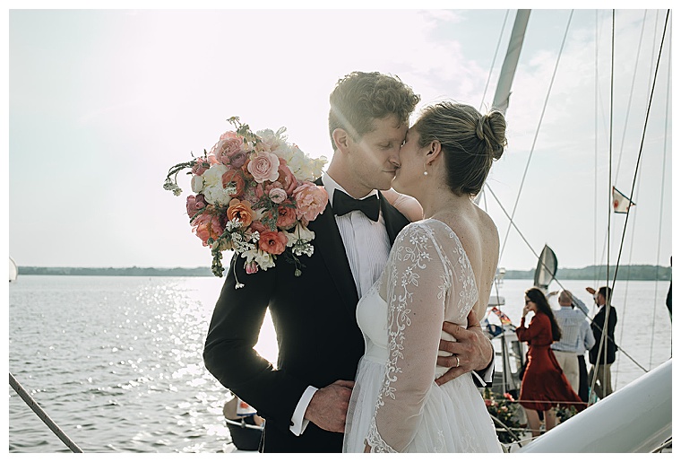The new husband and wife share a kiss on the bow of their ceremony sailboat as their fleet makes its way down the tred avon river