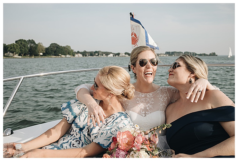 A blissful bride dressed in lace enjoys a sunset cruise with her new husband and family after their waterfront wedding ceremony