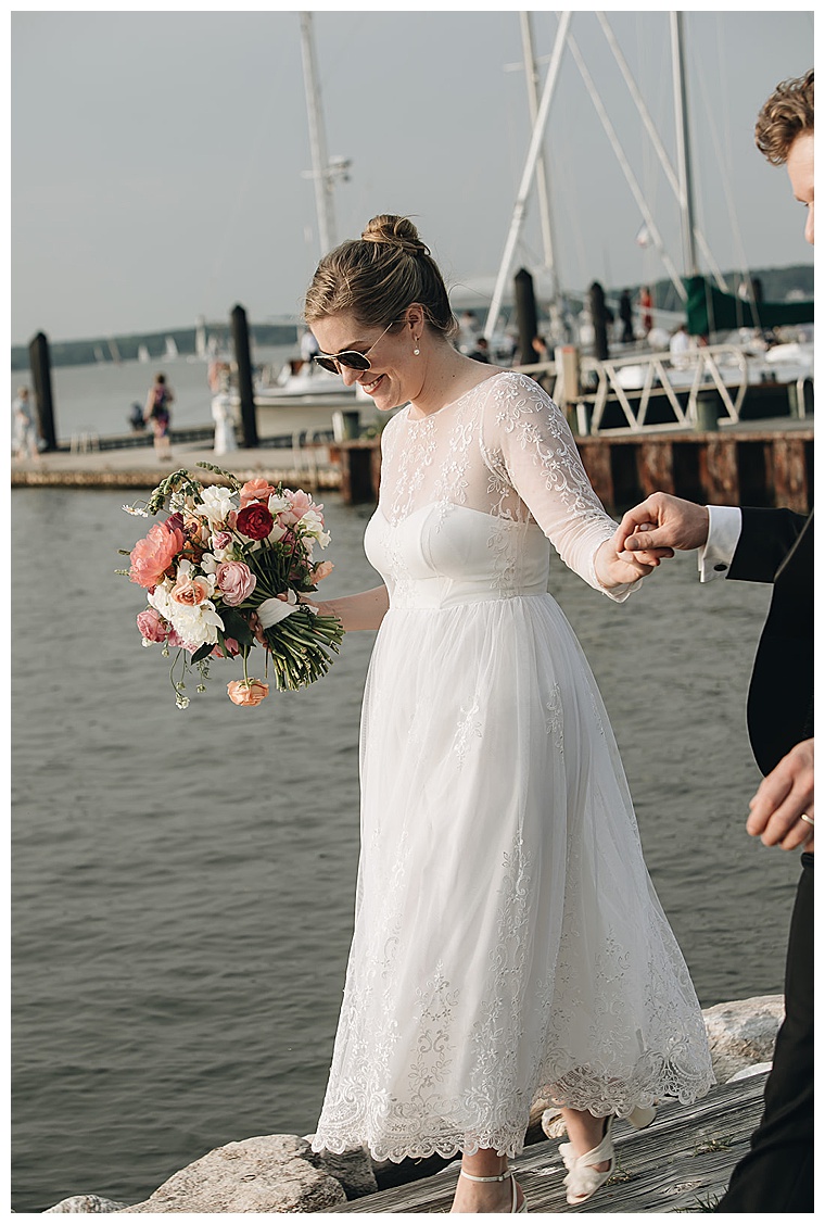 The groom helps his new bride off the sailboat and onto shore as they make their way to their romantic eastern shore wedding reception