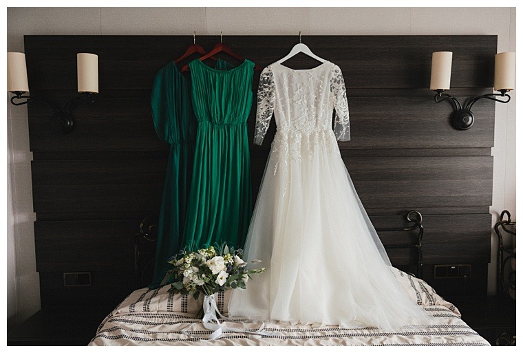 Modern bridal fashion. White wedding dress and green bridesmaids dresses hanging in the hotel room.