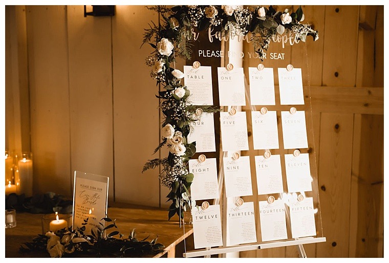 A custom seating chart sign with white roses and greenery