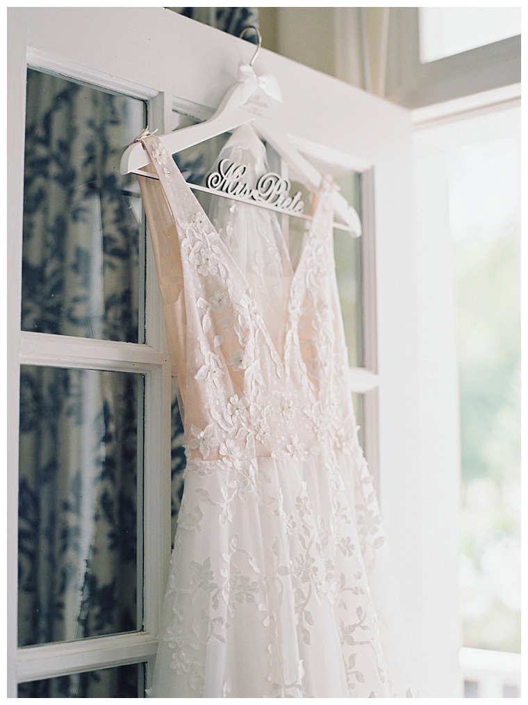 A lace, a-line bridal gown hangs on a custom bridal hanger as the bride gets ready for her ceremony