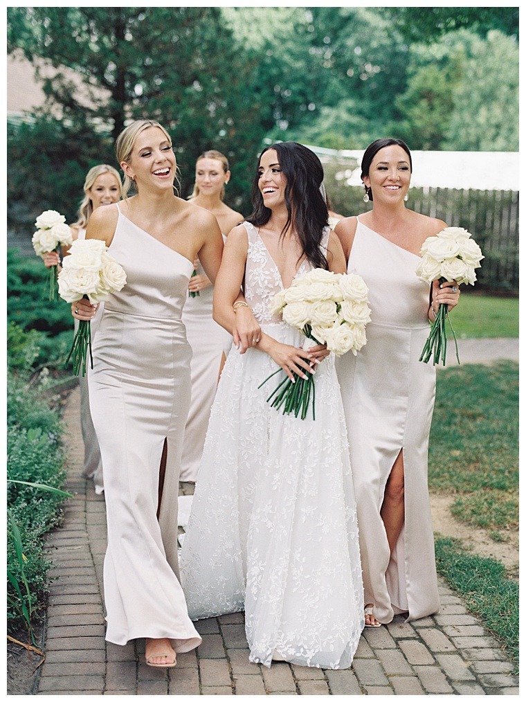 Bridesmaids dresses in champagne colored dresses escort the bride to the ceremony with beautiful bouquets of white roses