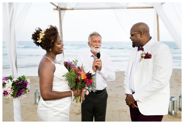 A beautiful beach wedding ceremony with the bride and groom smiling as the officiant leads the waterfront ceremony