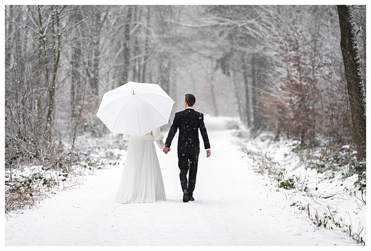 newlyweds in wedding dresses in the winter snowy forest on a walk with an umbrella.