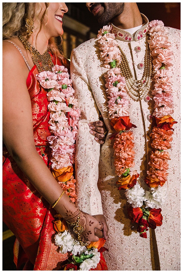 Gorgeous orange and pink florals adorn the bride and groom for their culturally infused wedding ceremony