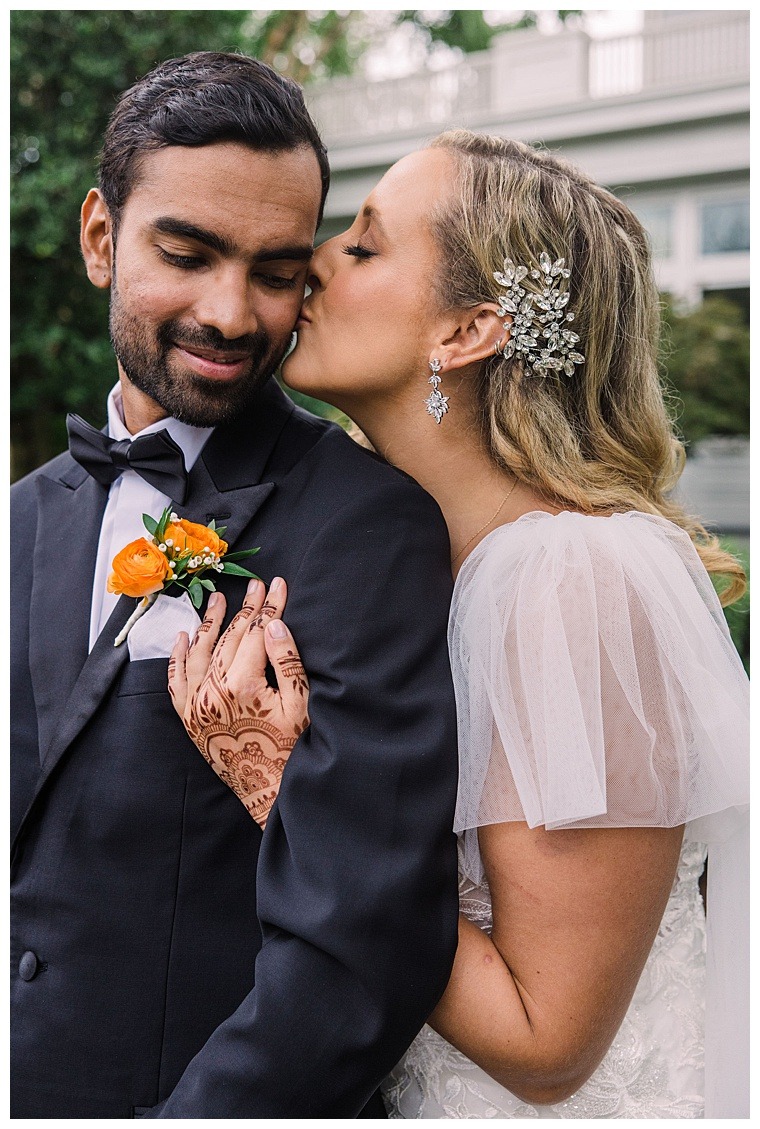 The bride is stunning in an elegant lace dress with a beaded hairpiece to match her gorgeous earrings as she kisses her new husband on the cheek