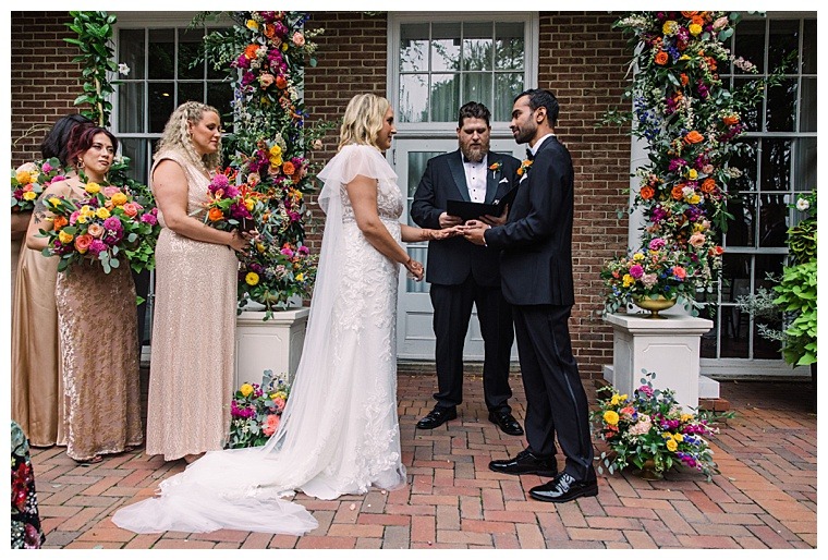 The bride and groom exchange vows under a colorful floral archway at The Tidewater Inn
