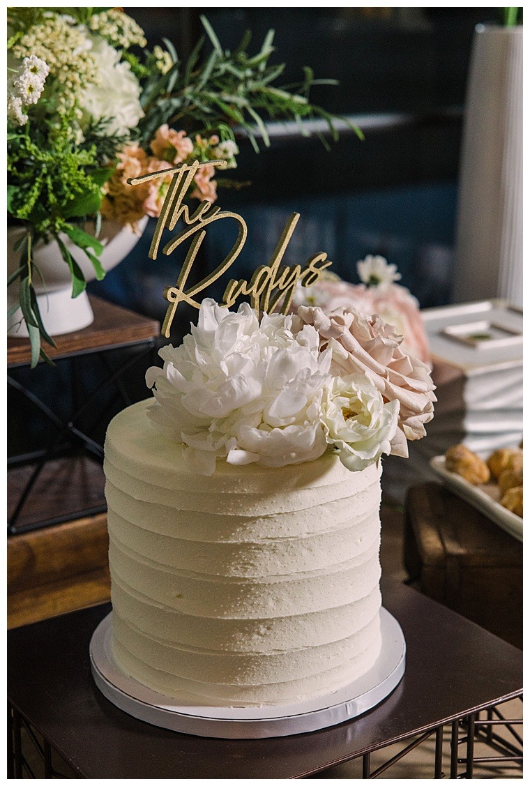 A single tiered wedding cake for the sweethearts to share is topped with a custom cake topper and pastel pink and white florals to match the details of the day