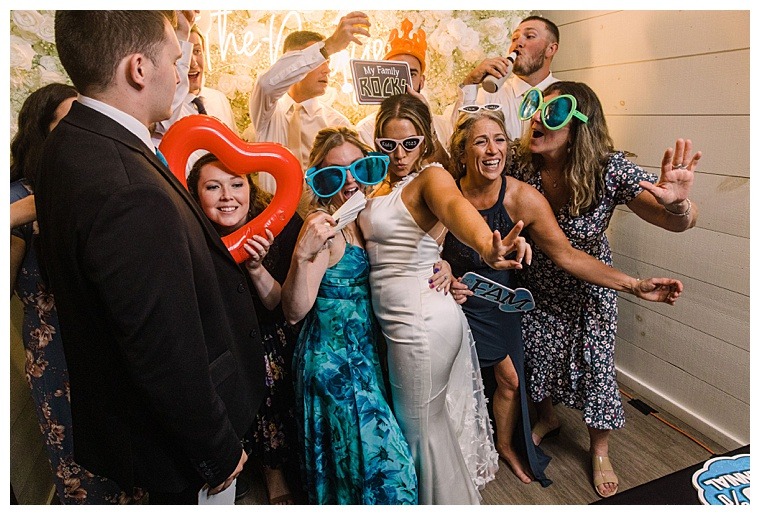 The bride and groom are surrounded by guests as they dance the night away and take silly wedding pictures in their fully stocked photobooth